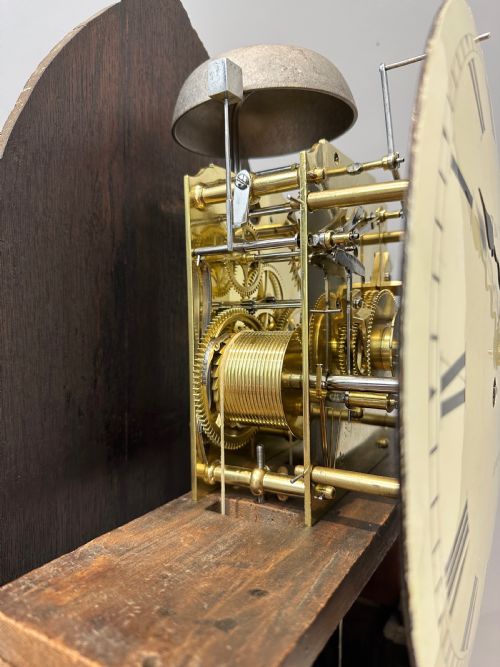 fig 4. A Regency flame mahogany longcase clock featuring a pointed arch hood, white circular dial signed by Thomas Wightman of London, and brass column details.