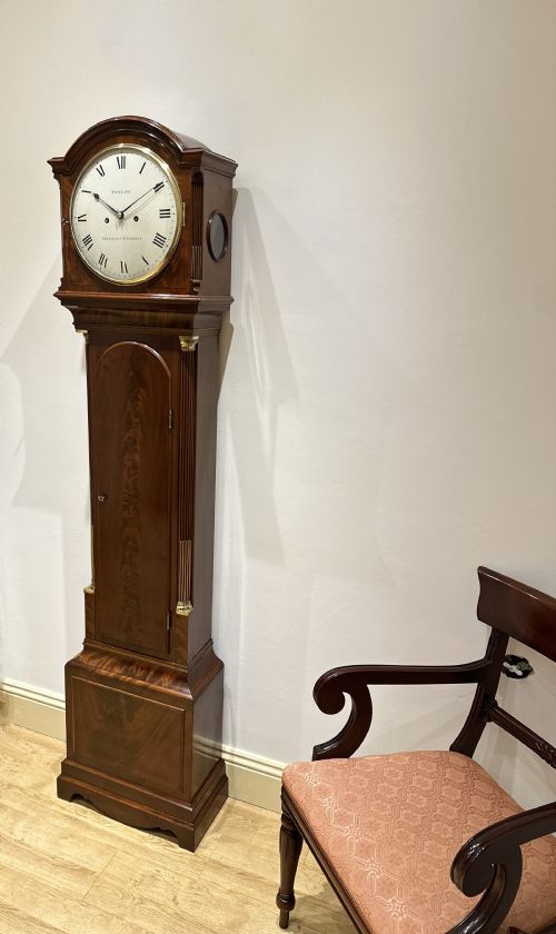 fig 4. A Georgian tall mahogany longcase clock featuring an arched hood, a circular dial with Roman numerals, and brass fluted quarter columns.