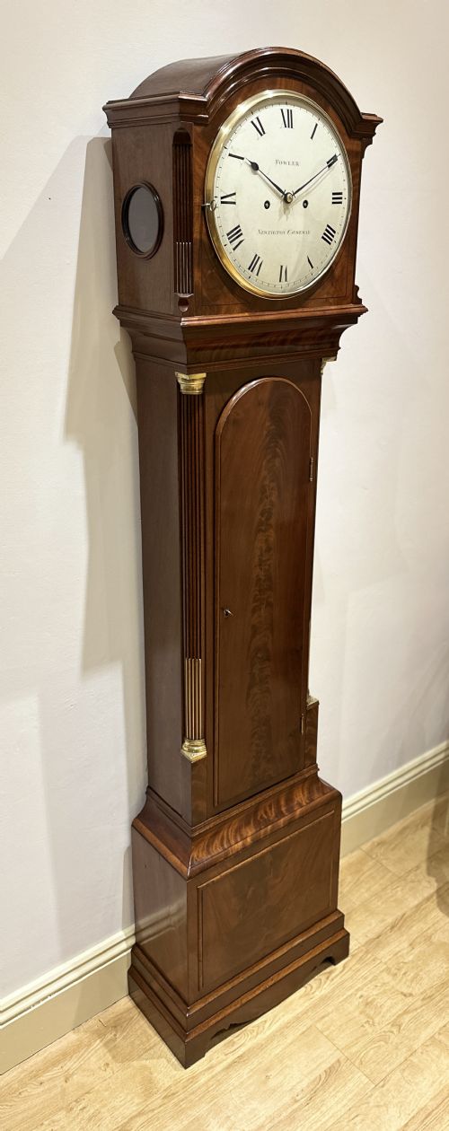 fig 5. A Georgian tall mahogany longcase clock featuring an arched hood, a circular dial with Roman numerals, and brass fluted quarter columns.