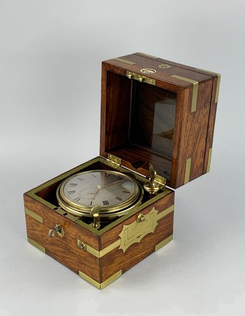 fig 1. An antique 19th-century brass-bound wooden box opening to reveal a gimballed marine chronometer clock with a silvered dial and Roman numerals.