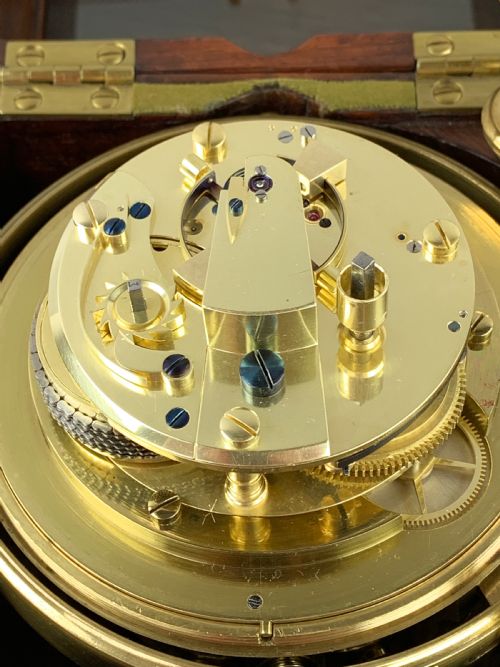 fig 2. An antique 19th-century brass-bound wooden box opening to reveal a gimballed marine chronometer clock with a silvered dial and Roman numerals.
