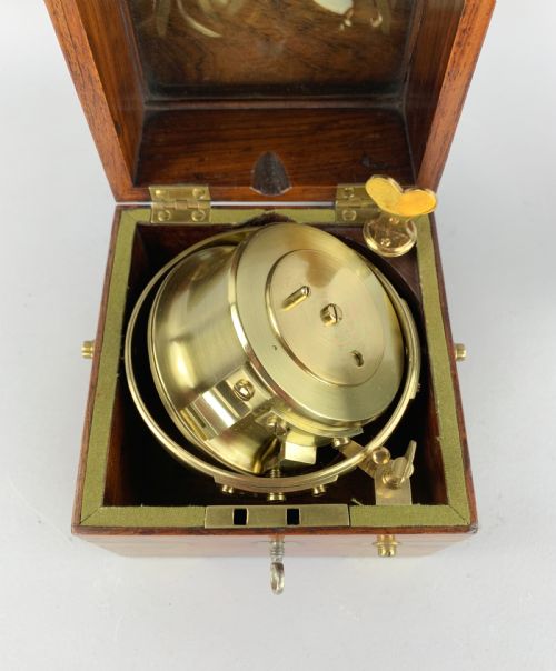 fig 6. An antique 19th-century brass-bound wooden box opening to reveal a gimballed marine chronometer clock with a silvered dial and Roman numerals.