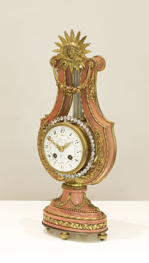 fig 1. A Louis XVI style lyre-shaped mantel clock featuring pink marble, gilt bronze ormolu mounts, and a central white enamel dial.
