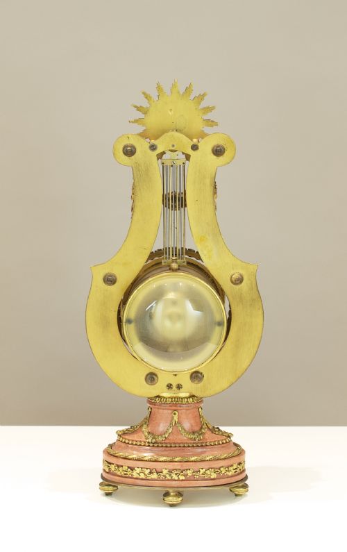 fig 4. A Louis XVI style lyre-shaped mantel clock featuring pink marble, gilt bronze ormolu mounts, and a central white enamel dial.