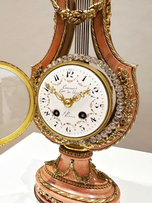 fig 5. A Louis XVI style lyre-shaped mantel clock featuring pink marble, gilt bronze ormolu mounts, and a central white enamel dial.