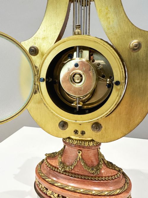 fig 6. A Louis XVI style lyre-shaped mantel clock featuring pink marble, gilt bronze ormolu mounts, and a central white enamel dial.