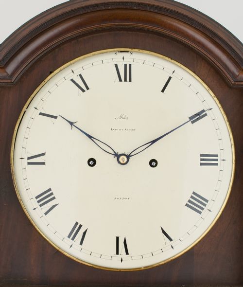 fig 4. A tall Georgian flame mahogany longcase clock featuring an arched hood, brass finial, and a circular white dial with Roman numerals.