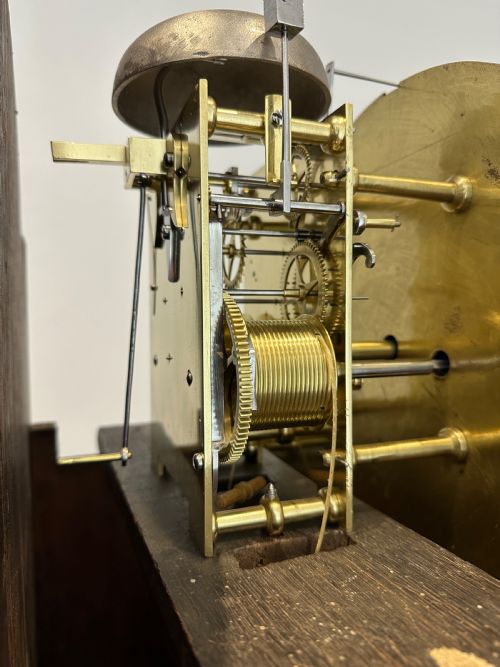 fig 6. A tall Georgian flame mahogany longcase clock featuring an arched hood, brass finial, and a circular white dial with Roman numerals.