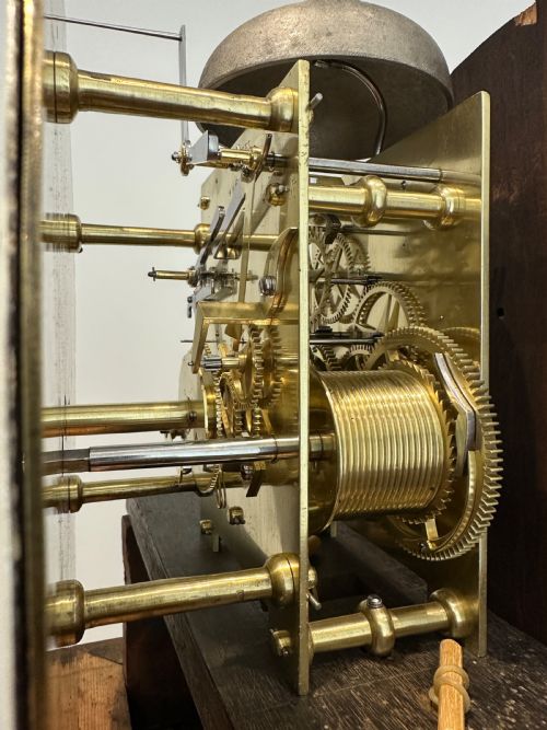 fig 8. A tall Georgian flame mahogany longcase clock featuring an arched hood, brass finial, and a circular white dial with Roman numerals.