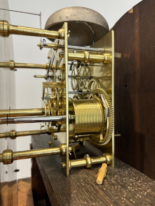 fig 9. A tall Georgian flame mahogany longcase clock featuring an arched hood, brass finial, and a circular white dial with Roman numerals.