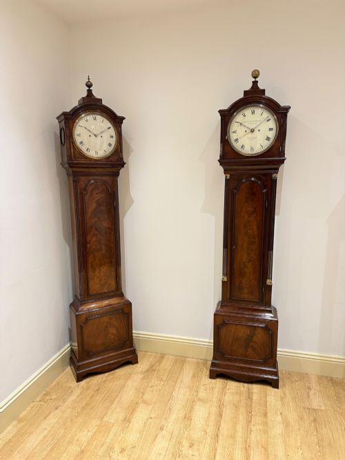 fig 4. A tall Georgian flame mahogany longcase clock featuring an arched dial hood topped with a brass ball finial, reeded side columns, and a shaped trunk door.