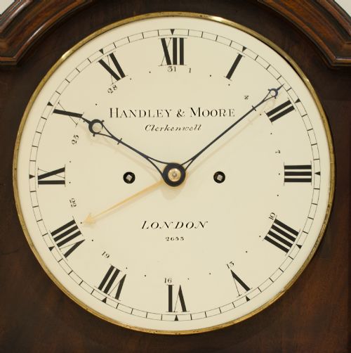 fig 5. A tall Georgian flame mahogany longcase clock featuring an arched dial hood topped with a brass ball finial, reeded side columns, and a shaped trunk door.