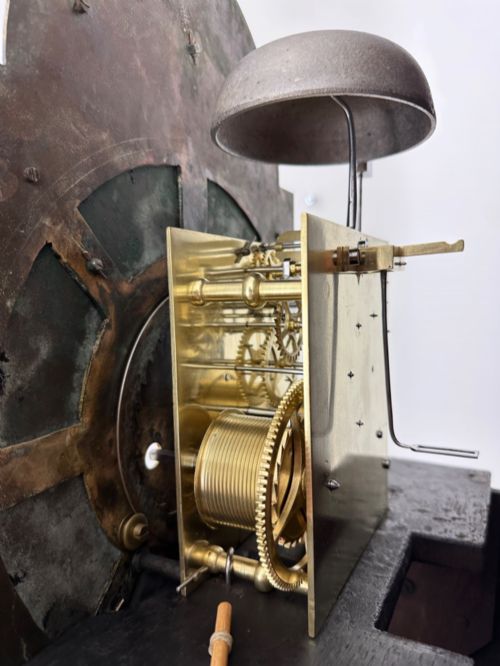 fig 5. An 18th-century Georgian longcase clock featuring a dark wooden cabinet, an arched hood with a finial, and a brass dial with silvered chapter ring.
