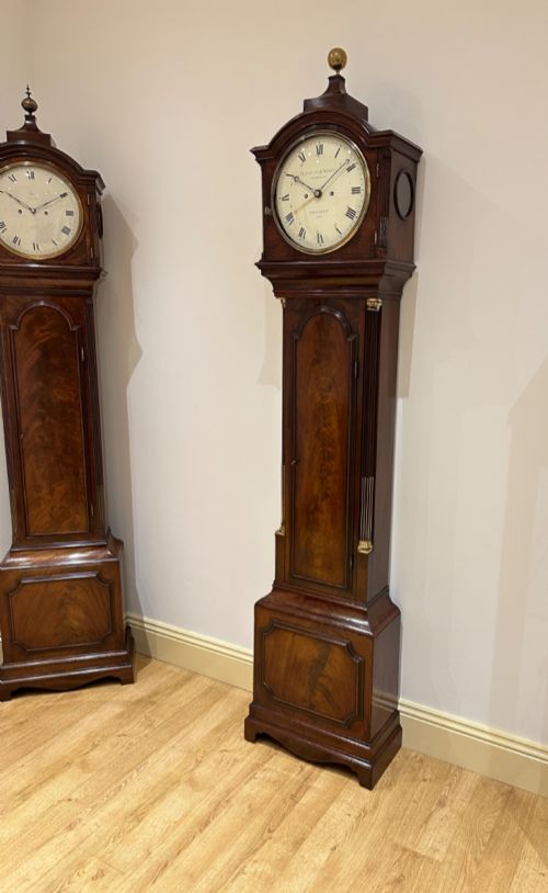 fig 1. A Georgian flame mahogany longcase clock featuring an arched bonnet top with a brass ball finial, reeded columns, and an enamelled circular dial signed Handley and Moore Clerkenwell London.
