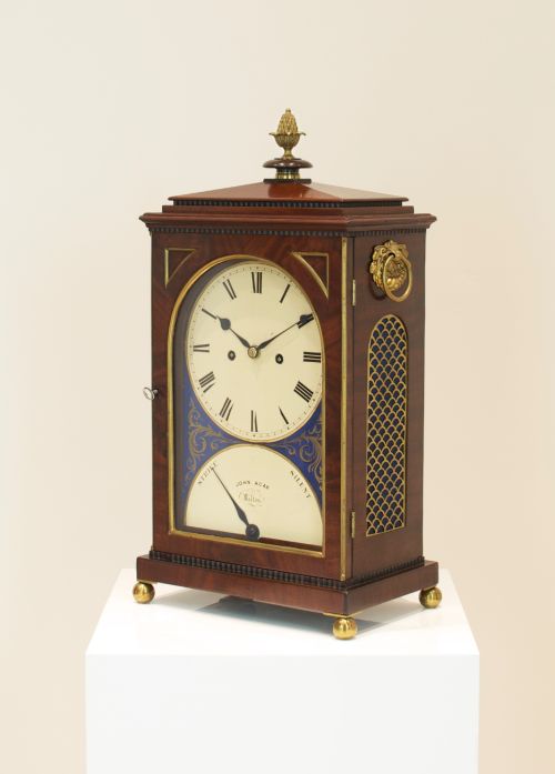 fig 2. A Georgian mahogany bracket clock featuring a brass pineapple finial, brass side handles, a white dial with Roman numerals, and a lower strike-silent mechanism.