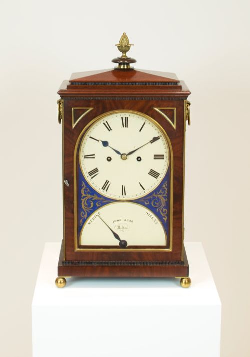 fig 3. A Georgian mahogany bracket clock featuring a brass pineapple finial, brass side handles, a white dial with Roman numerals, and a lower strike-silent mechanism.