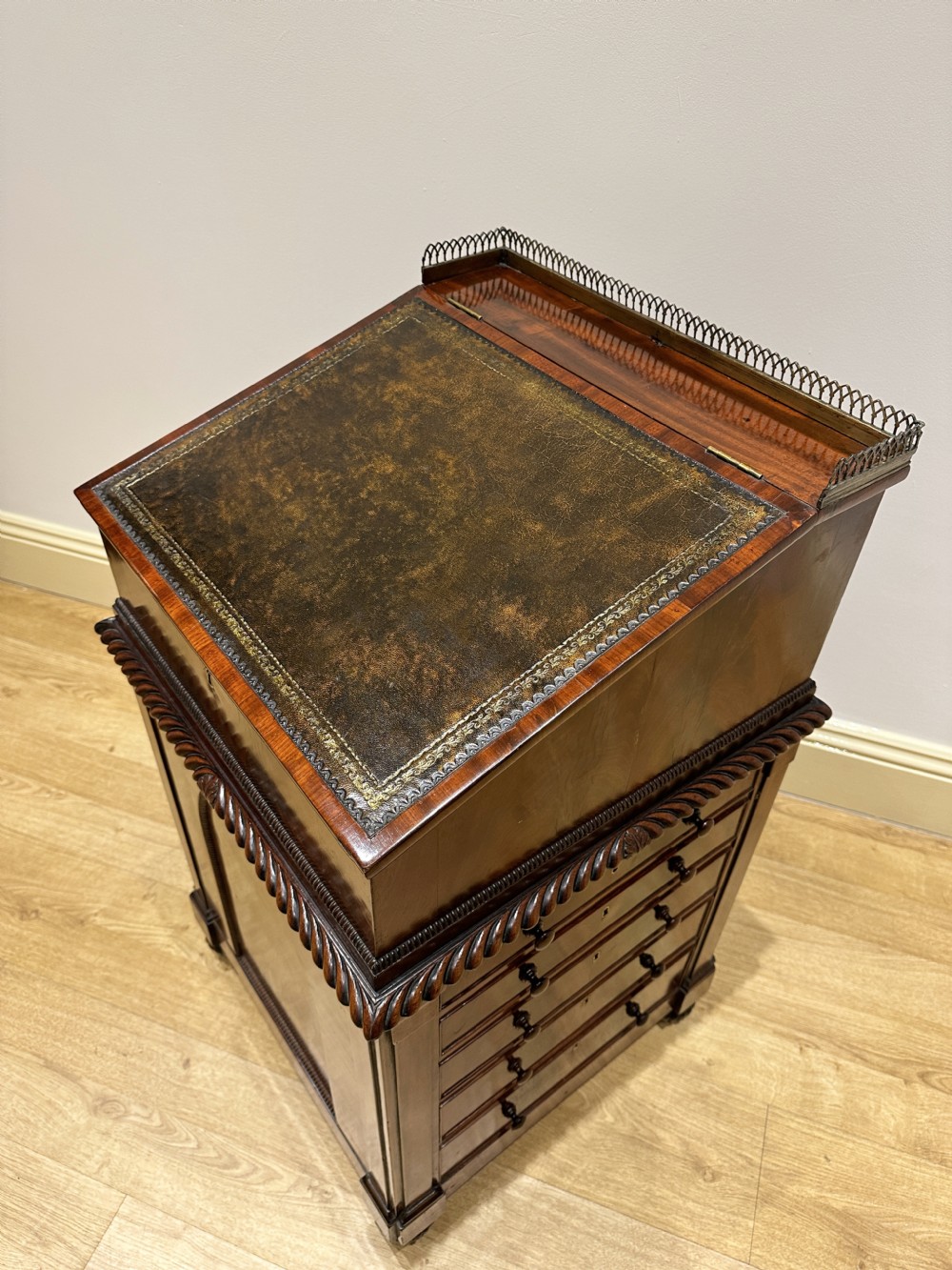 An antique Georgian mahogany Davenport desk featuring a sloped leather writing surface, decorative brass gallery, and side-mounted drawers. View V