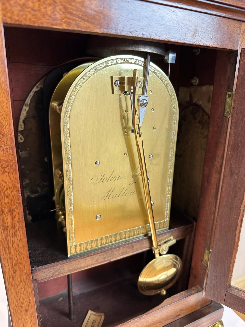 A Georgian mahogany bracket clock featuring a top brass pineapple finial, brass side handles, brass feet, and a arched dial signed John Agar Malton with a strike silent indicator. View XIII