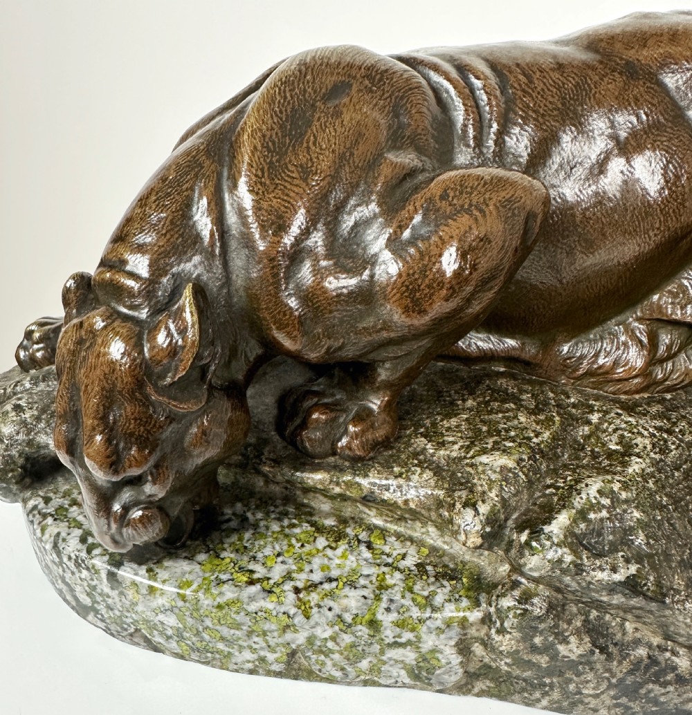 A patinated dark brown bronze sculpture depicting a crouching panther drinking water from a speckled grey stone base. View XII