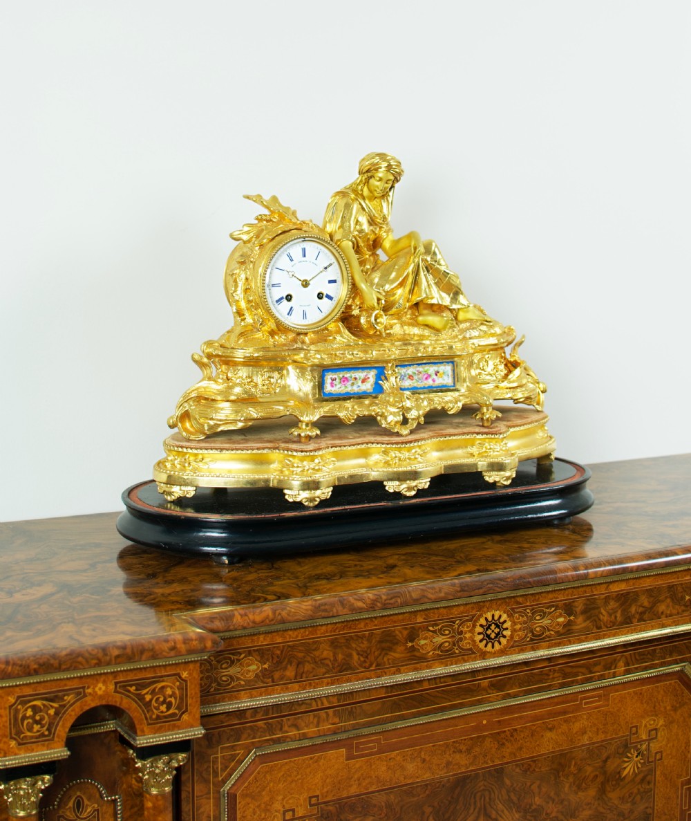 A nineteenth-century French gilt bronze mantel clock featuring a draped classical female figure beside a circular white dial with floral porcelain panels. View II