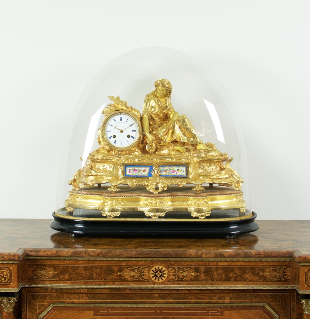 A nineteenth-century French gilt bronze mantel clock featuring a draped classical female figure beside a circular white dial with floral porcelain panels. View VI