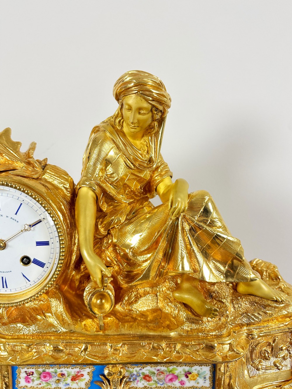 A nineteenth-century French gilt bronze mantel clock featuring a draped classical female figure beside a circular white dial with floral porcelain panels. View VII
