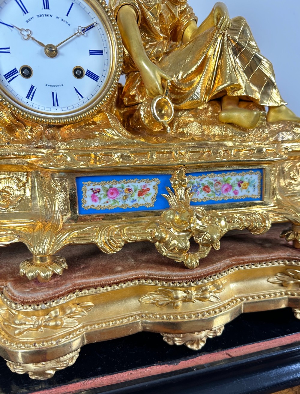A nineteenth-century French gilt bronze mantel clock featuring a draped classical female figure beside a circular white dial with floral porcelain panels. View VIII