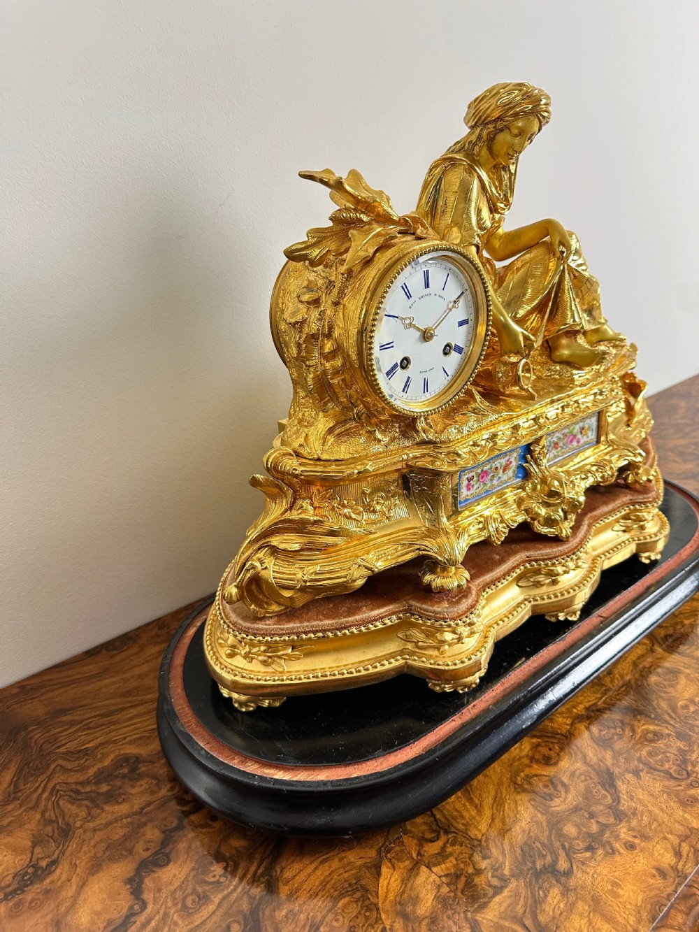 A nineteenth-century French gilt bronze mantel clock featuring a draped classical female figure beside a circular white dial with floral porcelain panels. View XI