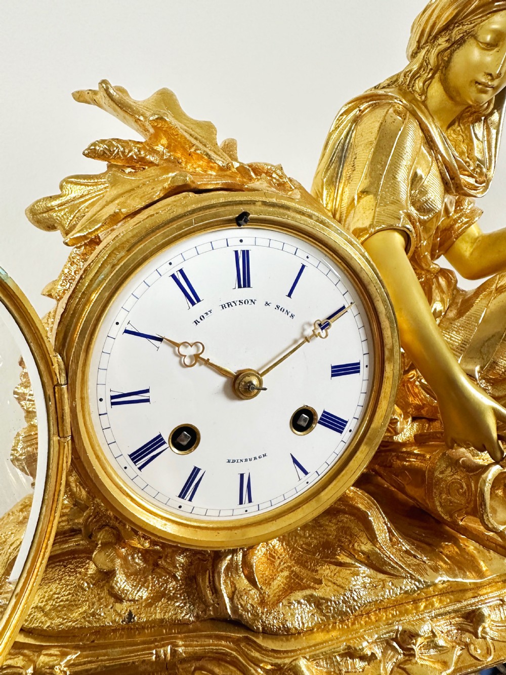 A nineteenth-century French gilt bronze mantel clock featuring a draped classical female figure beside a circular white dial with floral porcelain panels. View XII