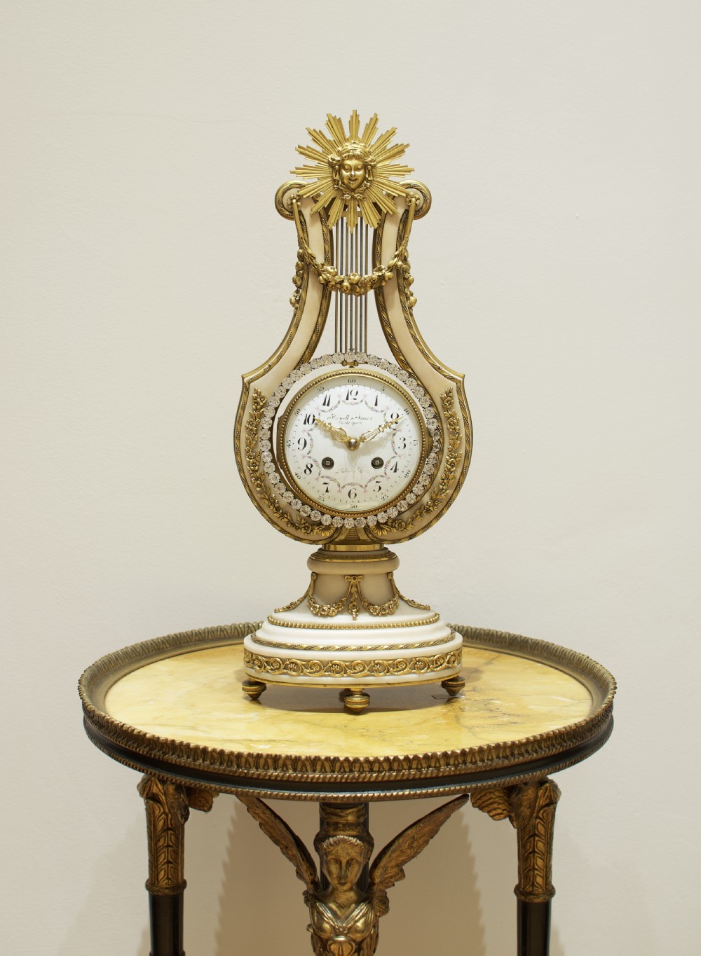 A Louis XVI style white marble and gilt bronze lyre-shaped mantel clock topped with a sunburst Apollo head mask and featuring a crystal-encrusted dial bezel. View II