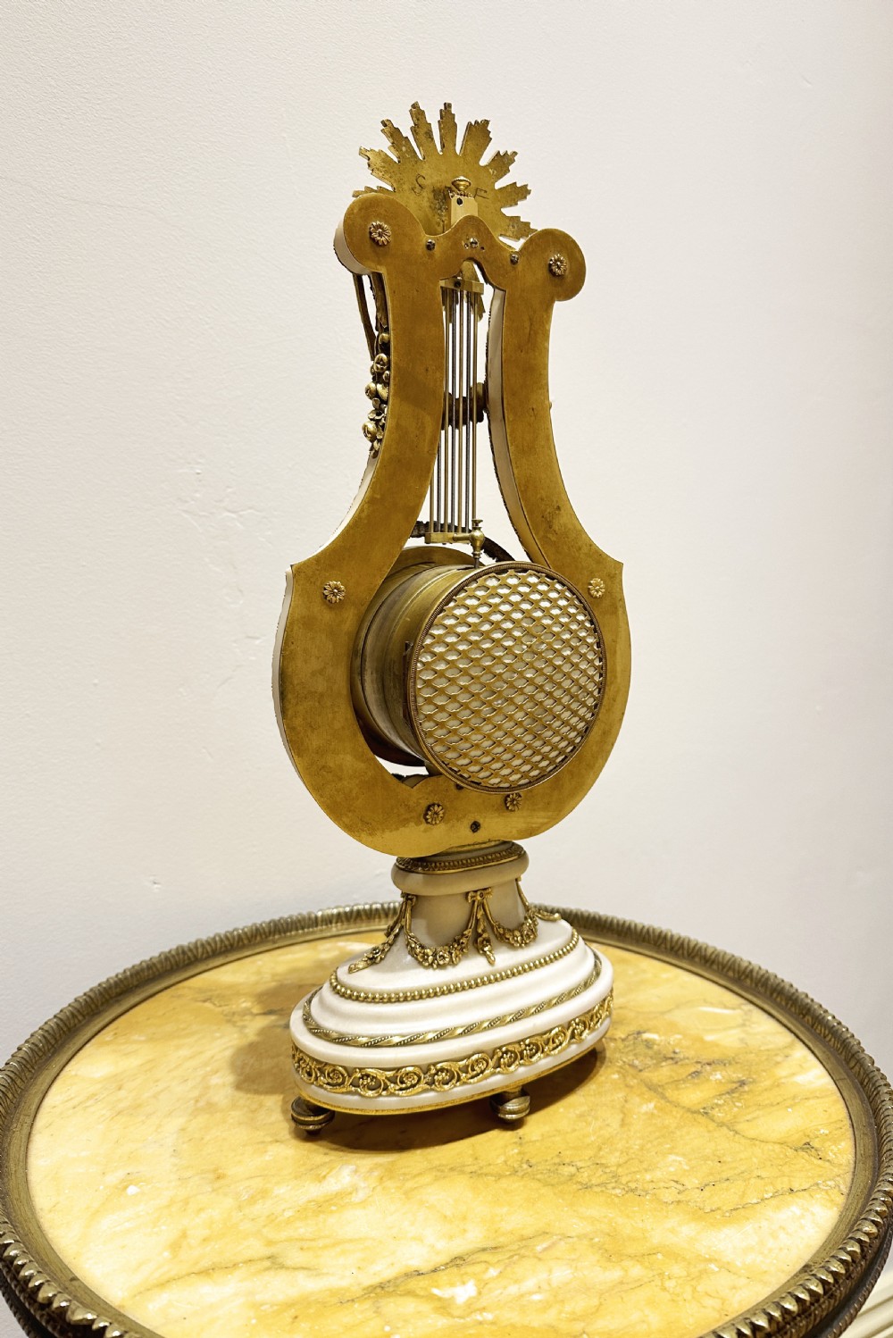 A Louis XVI style white marble and gilt bronze lyre-shaped mantel clock topped with a sunburst Apollo head mask and featuring a crystal-encrusted dial bezel. View VI