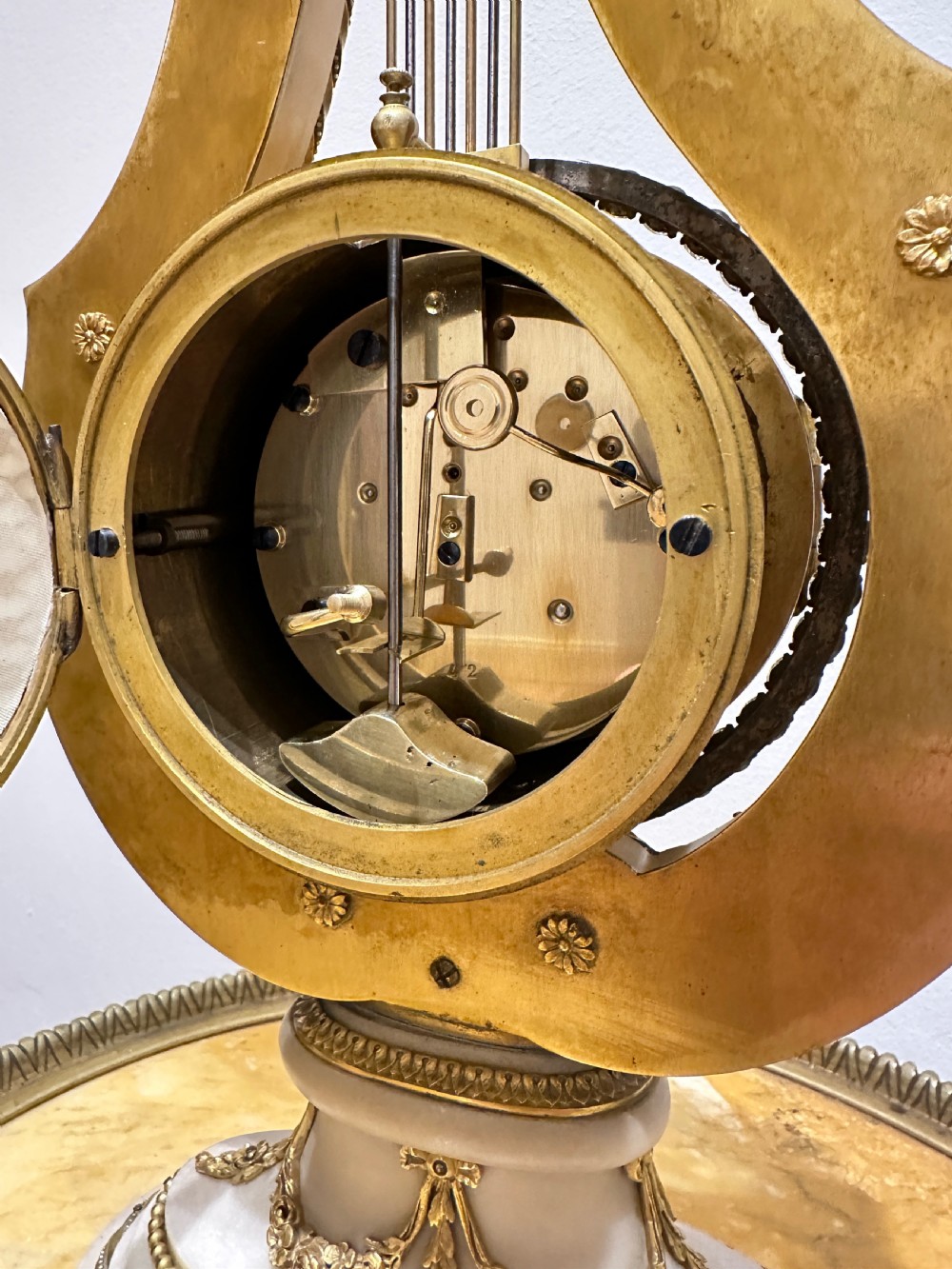 A Louis XVI style white marble and gilt bronze lyre-shaped mantel clock topped with a sunburst Apollo head mask and featuring a crystal-encrusted dial bezel. View VII