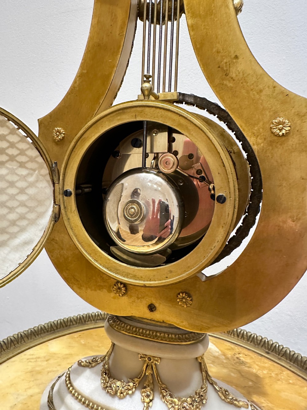 A Louis XVI style white marble and gilt bronze lyre-shaped mantel clock topped with a sunburst Apollo head mask and featuring a crystal-encrusted dial bezel. View IX