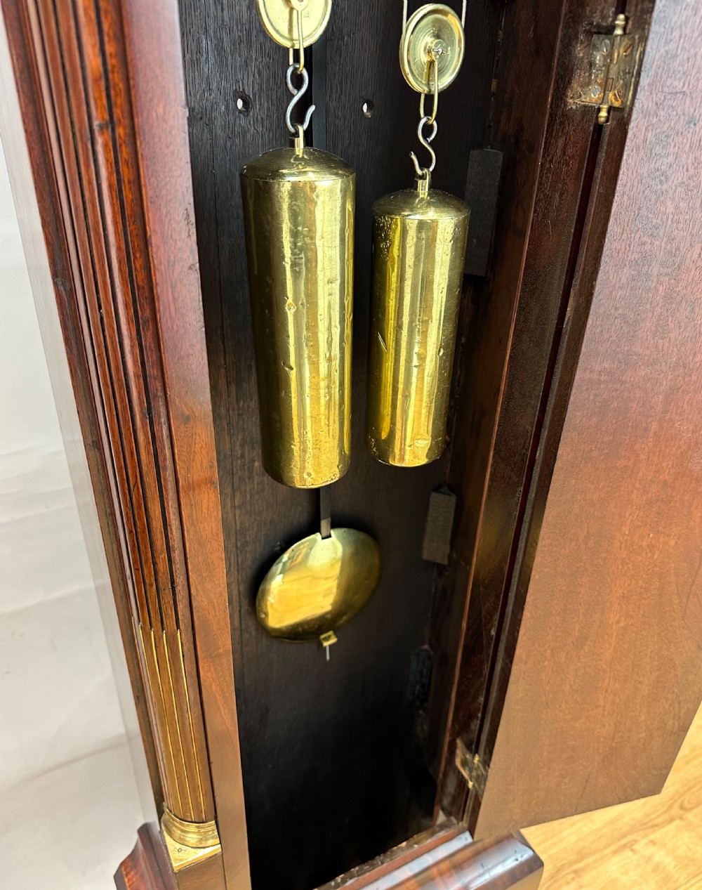 A Regency flame mahogany longcase clock featuring a pointed arch hood, white circular dial signed by Thomas Wightman of London, and brass column details. View X