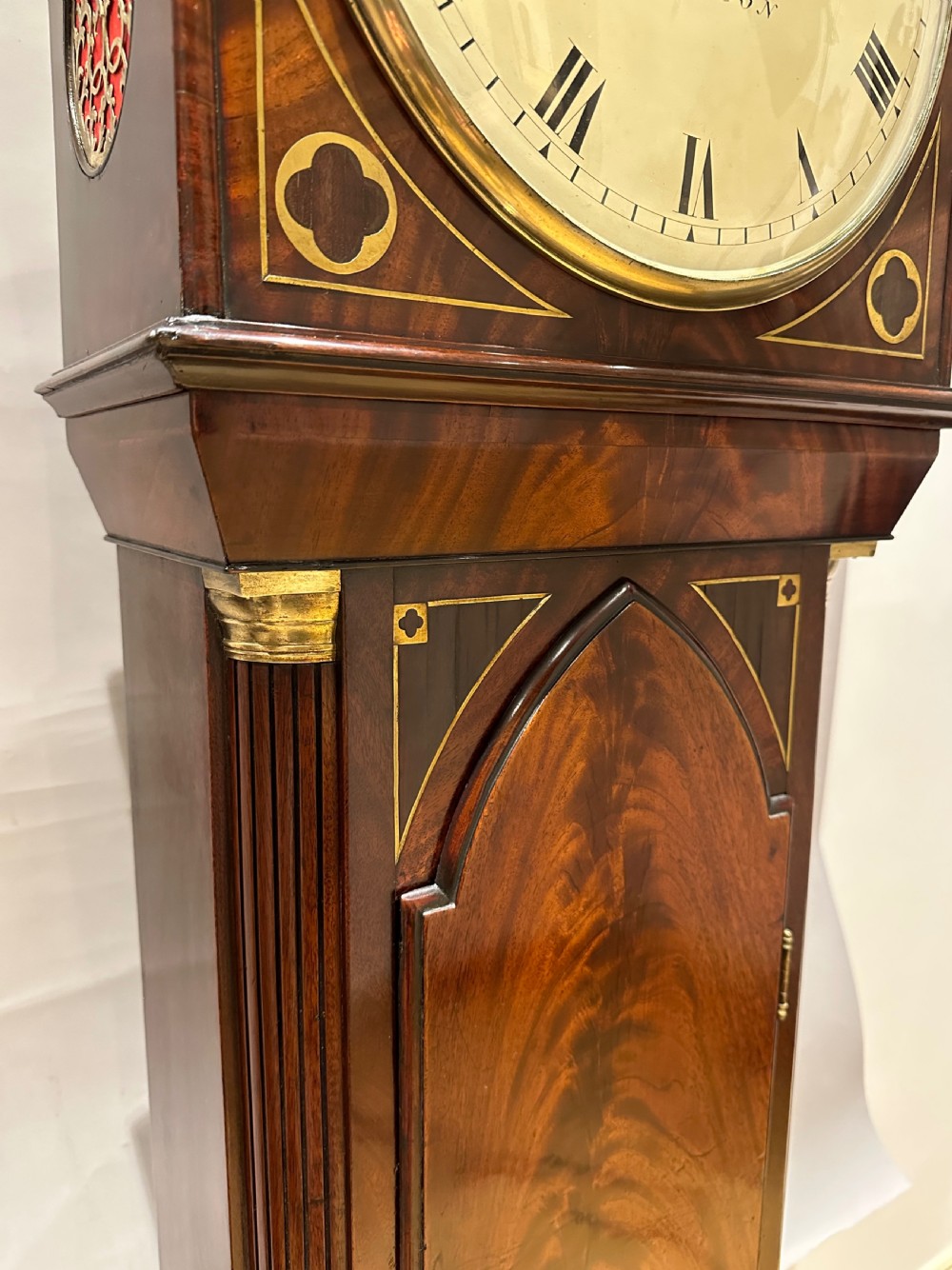 A Regency flame mahogany longcase clock featuring a pointed arch hood, white circular dial signed by Thomas Wightman of London, and brass column details. View XI