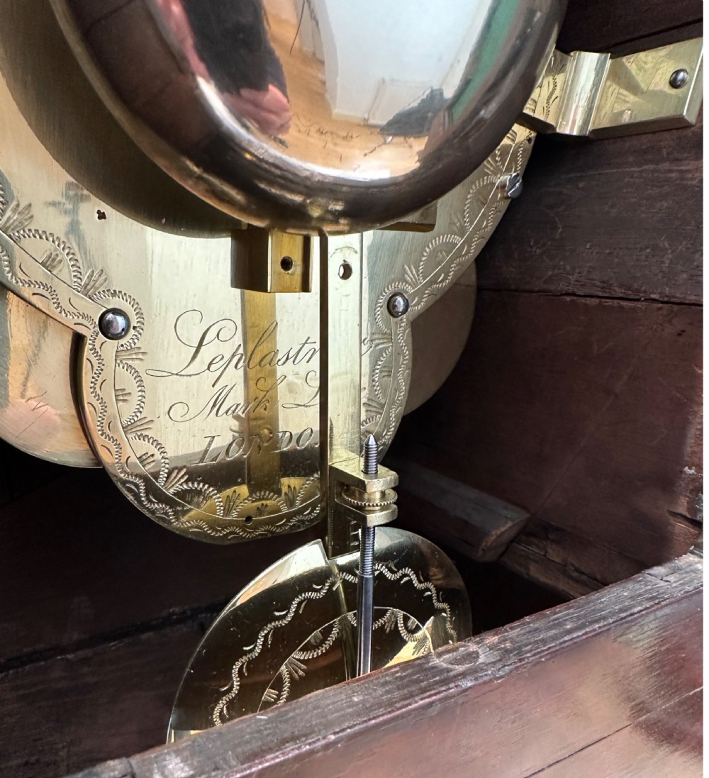 A Regency mahogany and brass bracket clock featuring a round white dial with Roman numerals, topped with a brass pineapple finial and resting on ball feet. View VI
