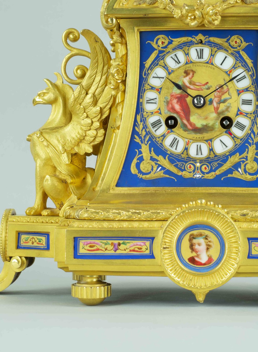 A French ormolu mantel clock featuring a classical female bust finial, blue enamel dial, and flanked by winged griffins on an ornate base. View III