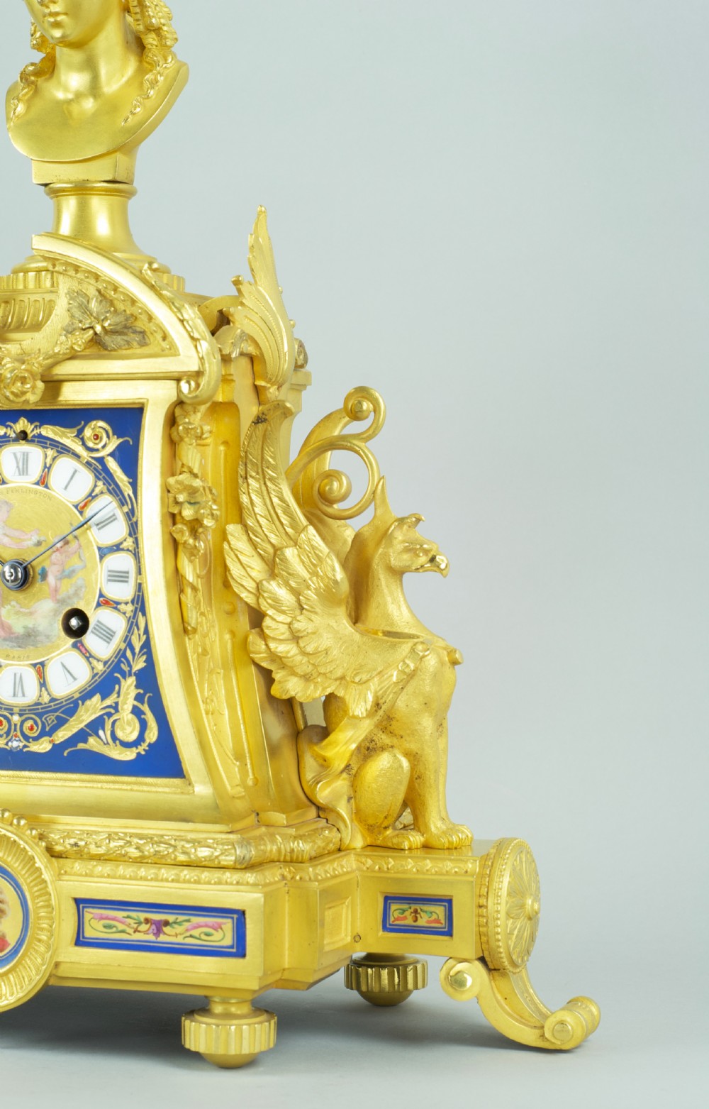 A French ormolu mantel clock featuring a classical female bust finial, blue enamel dial, and flanked by winged griffins on an ornate base. View V