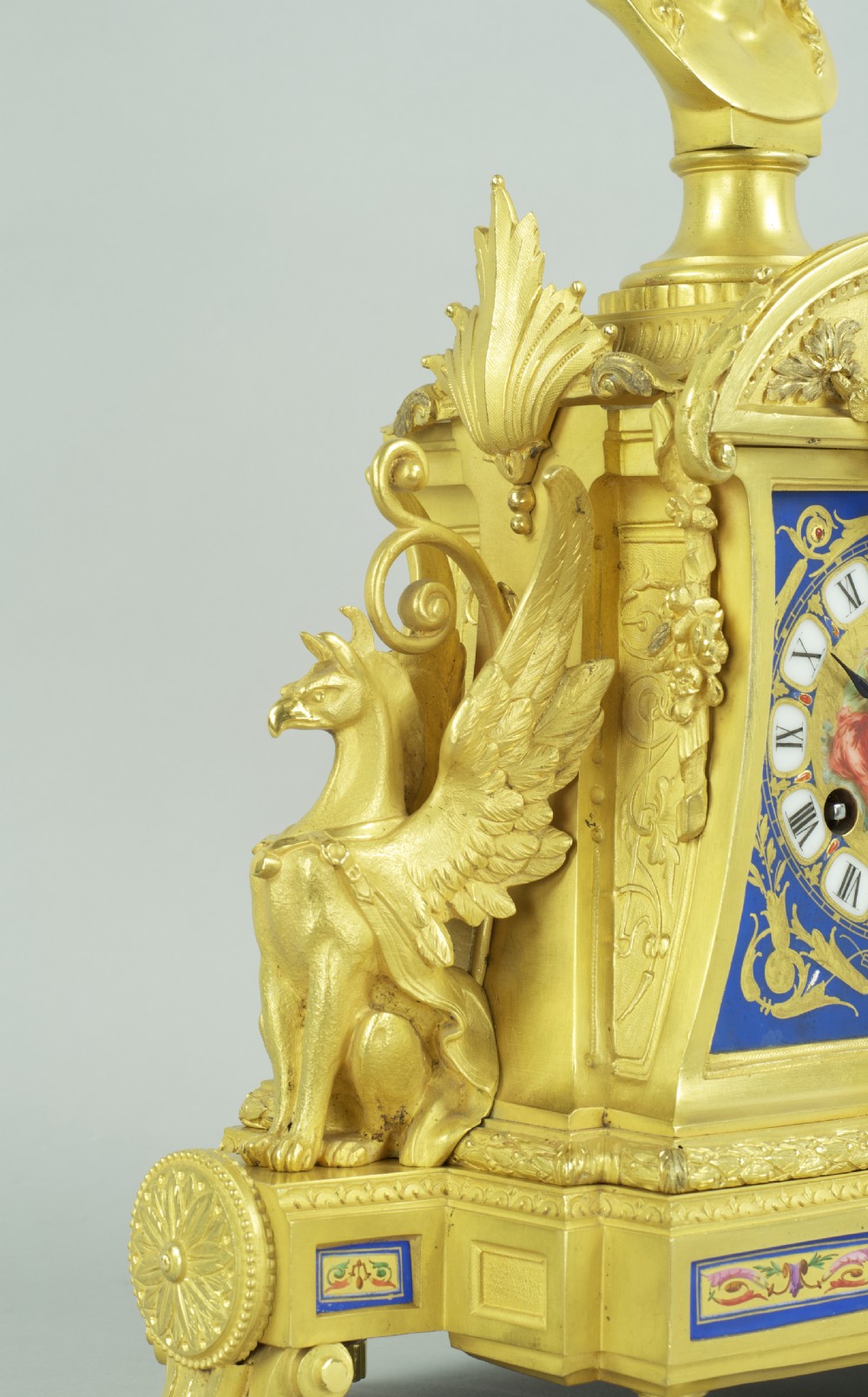 A French ormolu mantel clock featuring a classical female bust finial, blue enamel dial, and flanked by winged griffins on an ornate base. View VI
