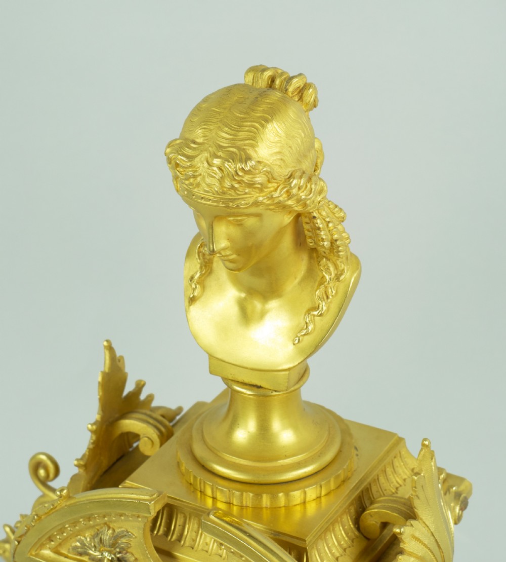 A French ormolu mantel clock featuring a classical female bust finial, blue enamel dial, and flanked by winged griffins on an ornate base. View VIII