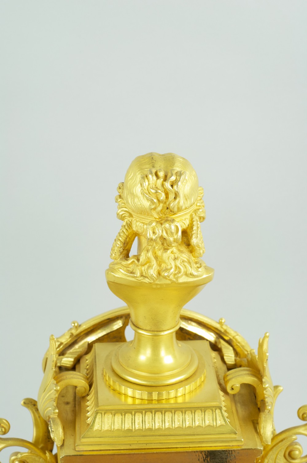 A French ormolu mantel clock featuring a classical female bust finial, blue enamel dial, and flanked by winged griffins on an ornate base. View IX
