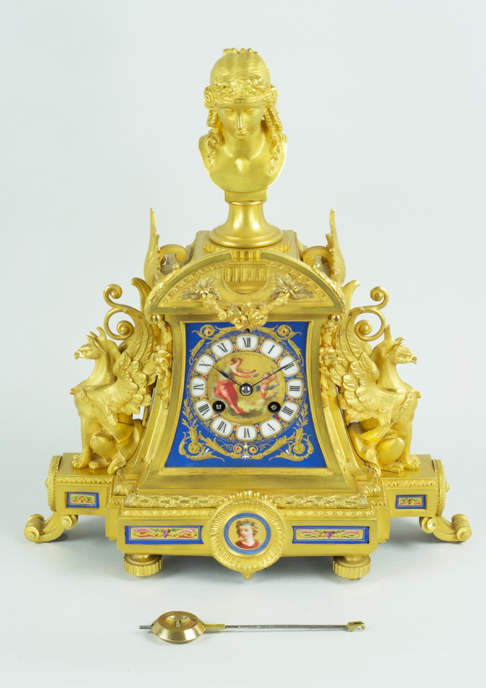 A French ormolu mantel clock featuring a classical female bust finial, blue enamel dial, and flanked by winged griffins on an ornate base. View XII