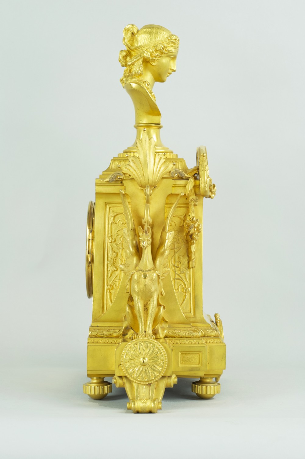 A French ormolu mantel clock featuring a classical female bust finial, blue enamel dial, and flanked by winged griffins on an ornate base. View XIV