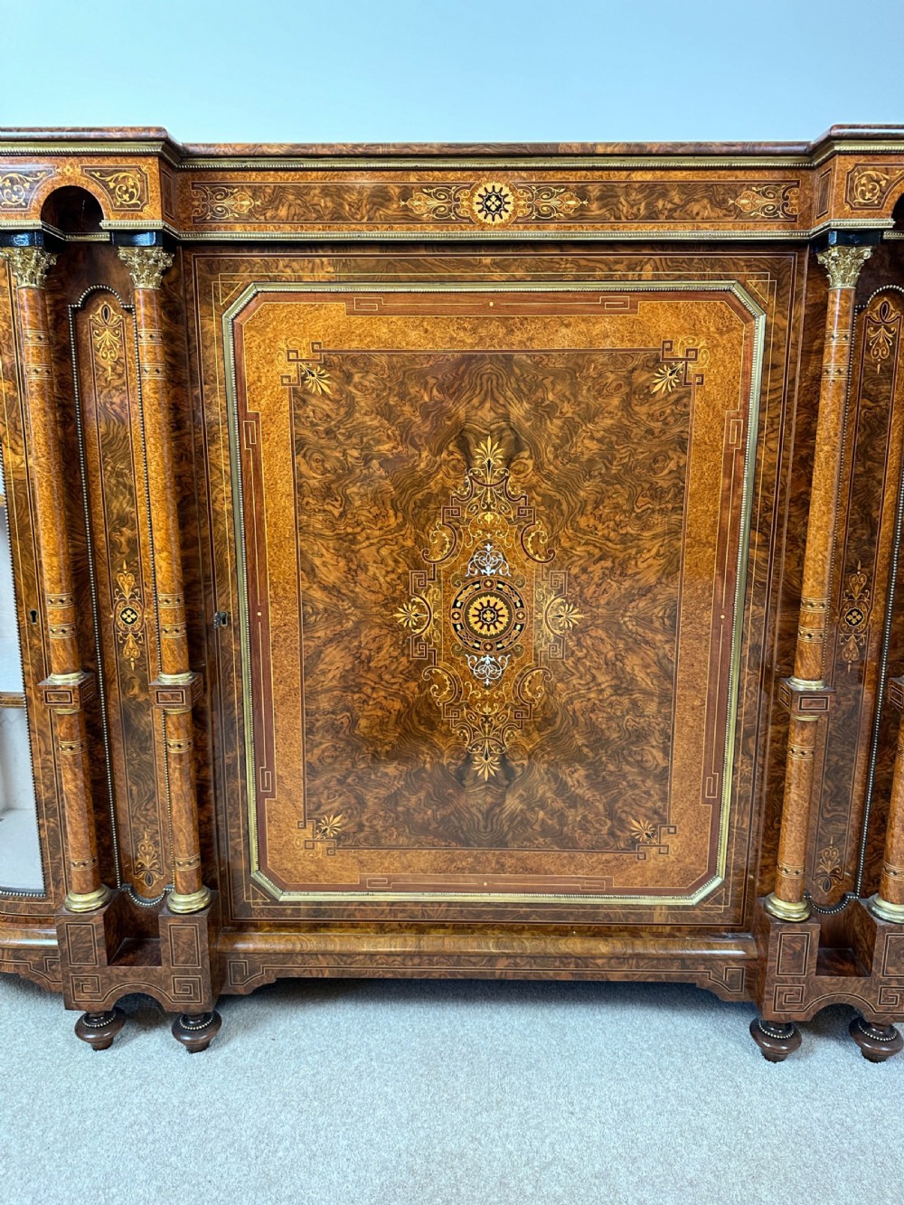 A Victorian burr walnut credenza sideboard featuring intricate marquetry inlay, a central panelled cupboard door, two curved glass display doors, and gilt brass mounts. View XIV
