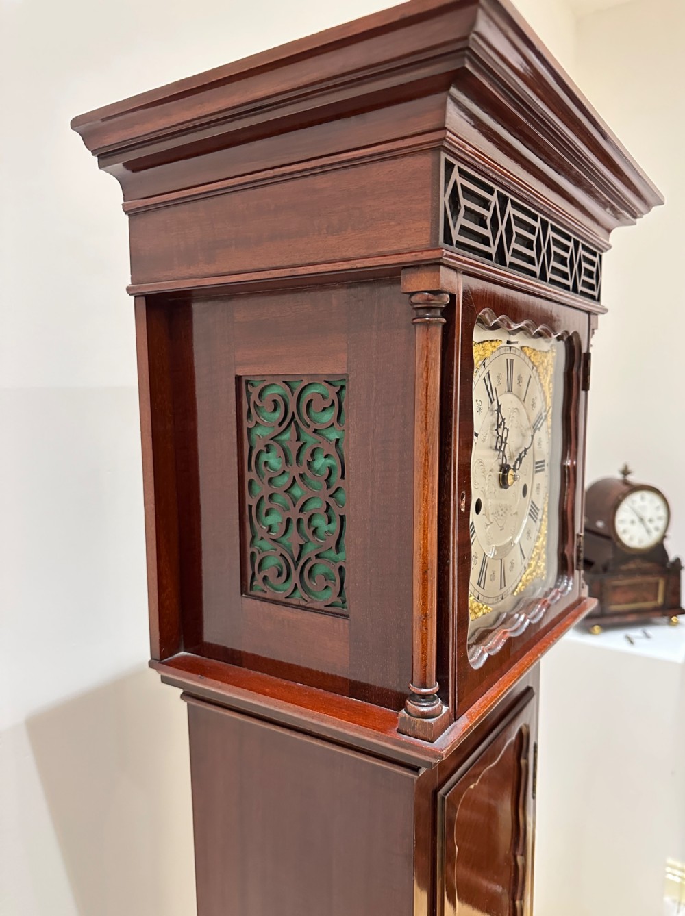 A tall mahogany grandmother clock featuring a brass and silvered dial with Roman numerals, geometric carved mouldings, and bracket feet. View XIII