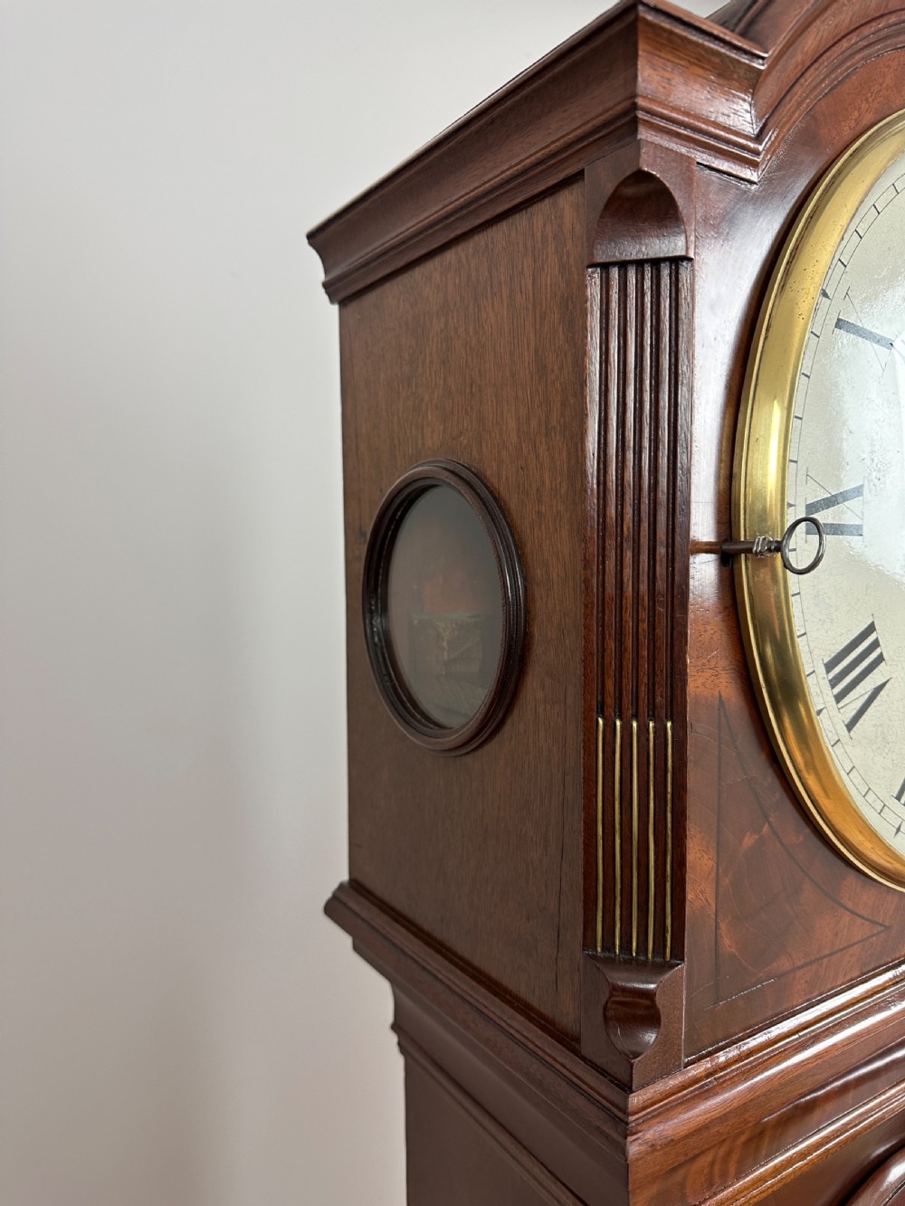 A Georgian tall mahogany longcase clock featuring an arched hood, a circular dial with Roman numerals, and brass fluted quarter columns. View XII