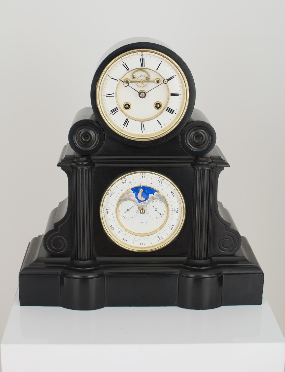 An antique black slate French mantel clock featuring two stacked circular dials, including an upper time display with Roman numerals and a lower perpetual calendar with a moonphase indicator. View V