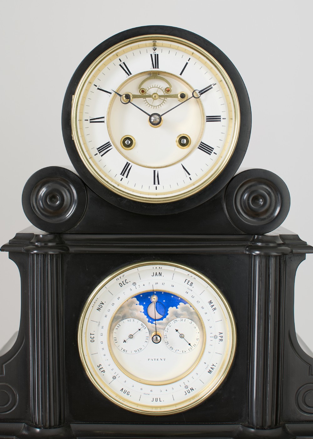 An antique black slate French mantel clock featuring two stacked circular dials, including an upper time display with Roman numerals and a lower perpetual calendar with a moonphase indicator. View II