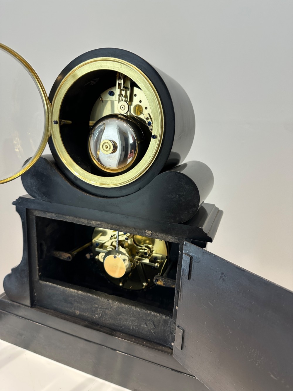 An antique black slate French mantel clock featuring two stacked circular dials, including an upper time display with Roman numerals and a lower perpetual calendar with a moonphase indicator. View XII