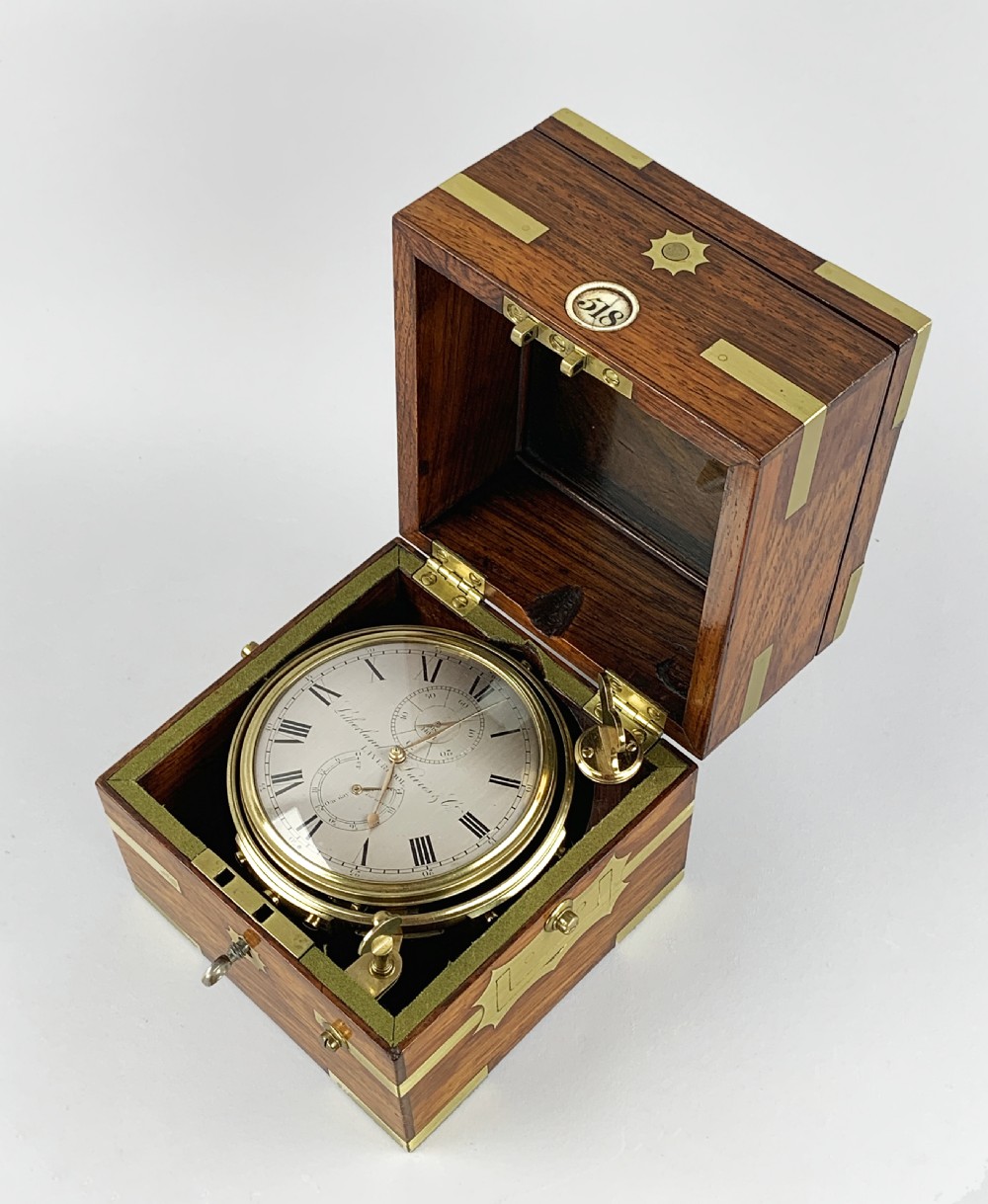 An antique 19th-century brass-bound wooden box opening to reveal a gimballed marine chronometer clock with a silvered dial and Roman numerals.